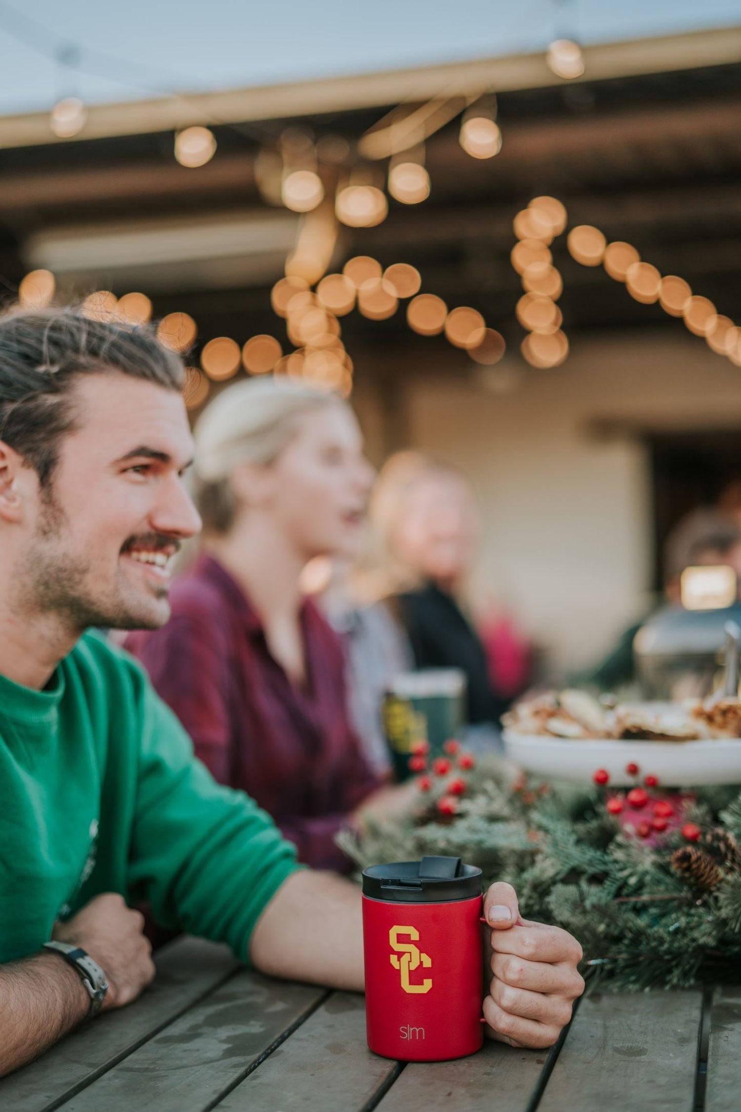 Warm golden string lights creating soft bokeh in background with vibrant red drinkware in sharp focus in foreground
