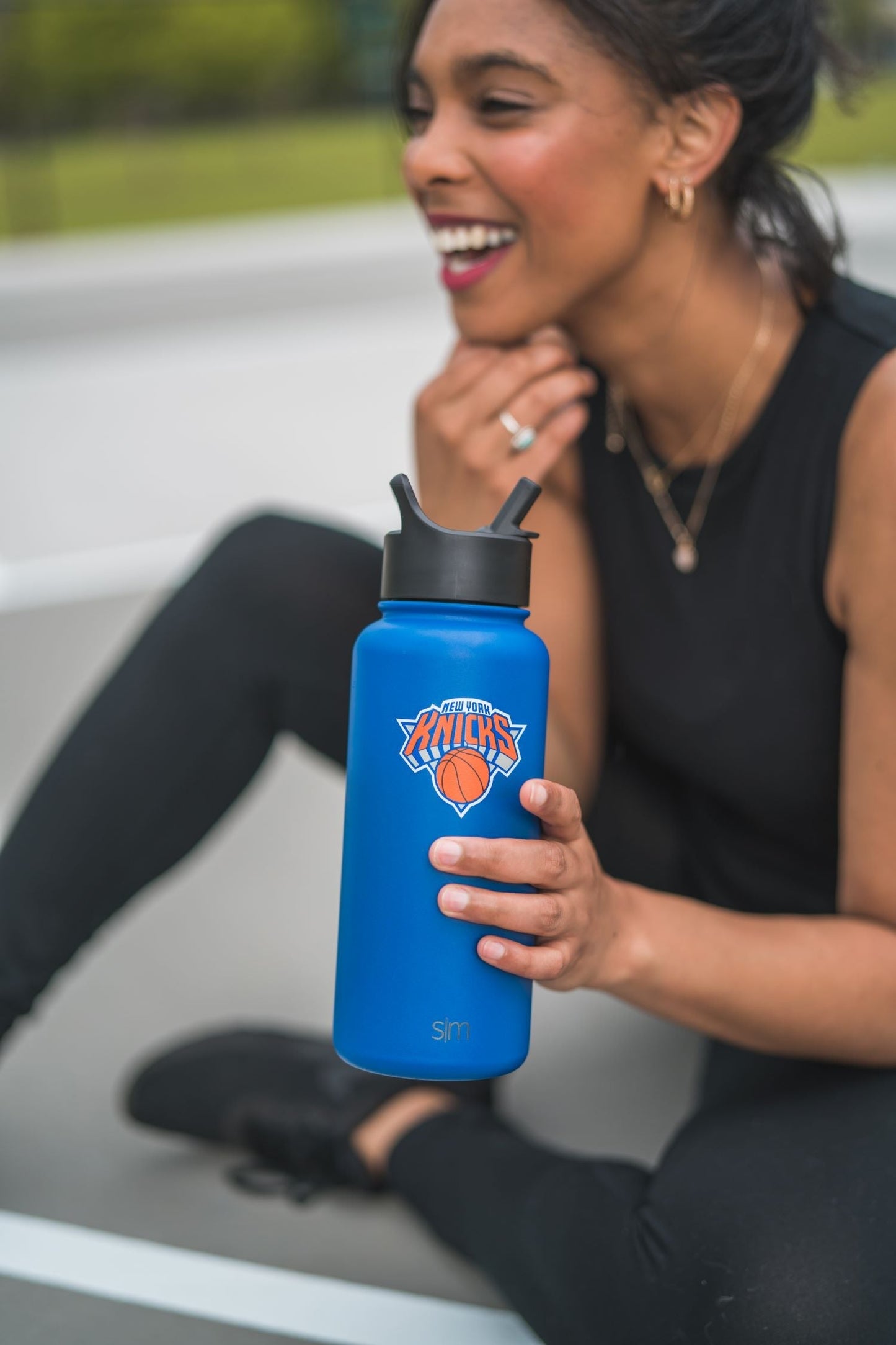 Person holding a vibrant royal blue water bottle, wearing black clothing against a neutral background
