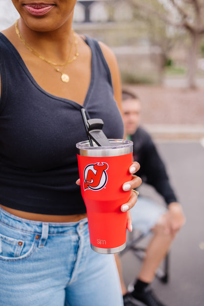 Person holding a bright red tumbler wearing a navy sleeveless top