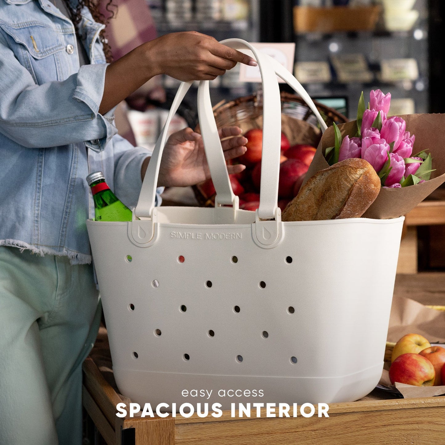 White Simple Modern Getaway Bag filled with fresh groceries including flowers, bread, and produce, held by a person in a denim jacket, demonstrating spacious interior and easy access.