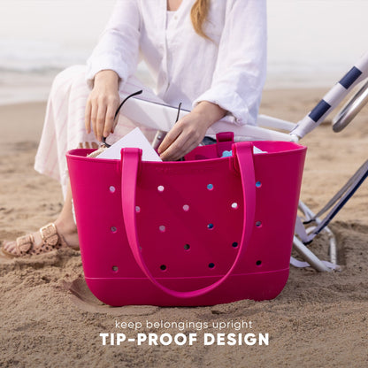 Hot pink tip-proof beach tote bag with perforated design being packed by woman in white linen on sandy beach, with text "keep belongings upright TIP-PROOF DESIGN"