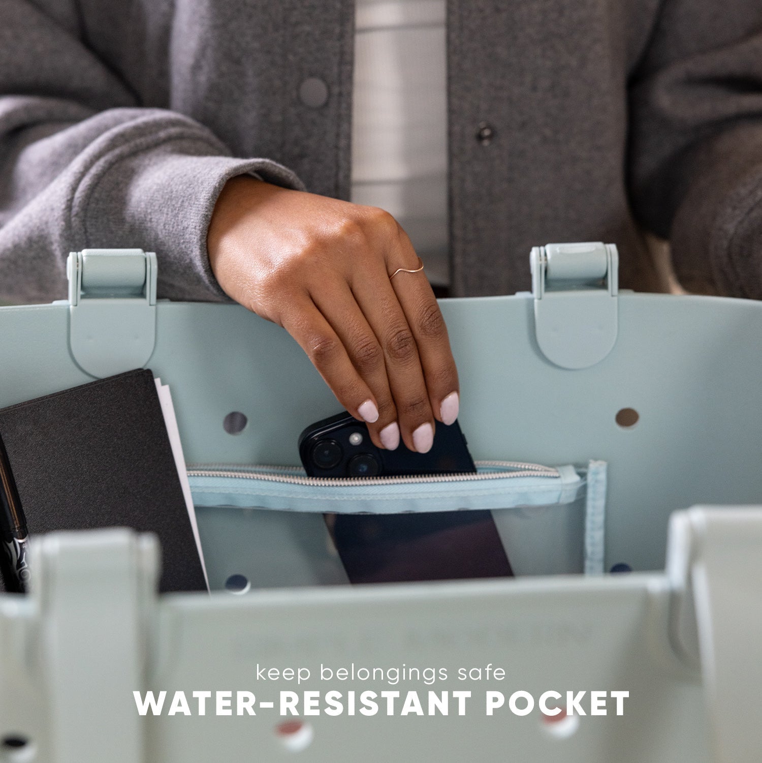 Person placing black smartphone into water-resistant pocket of sage green getaway bag. Text reads "keep belongings safe" and "WATER-RESISTANT POCKET."