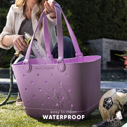 Lavender waterproof tote bag displayed on woman wearing white cardigan, shown with water to demonstrate water-resistant feature.
