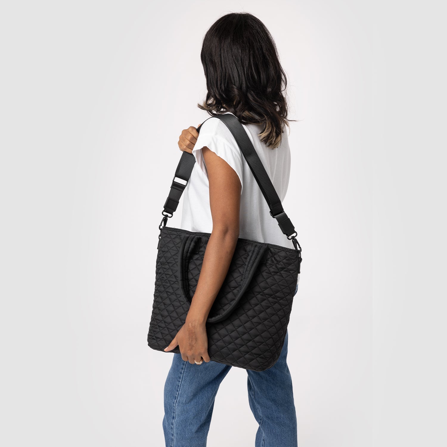 Quilted Harper Bag in denim blue with quilted texture, displayed against light gray background. Black handles and white accent details visible on structured handbag design.