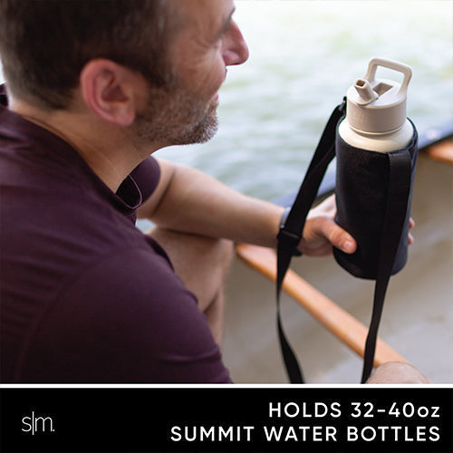 Man in burgundy t-shirt holding Simple Modern water bottle carrier with black neoprene sleeve and white tan plastic handle near water